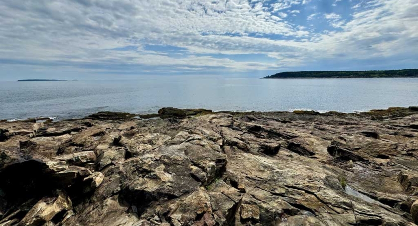 A rocky shore lies before a blue body of water. 